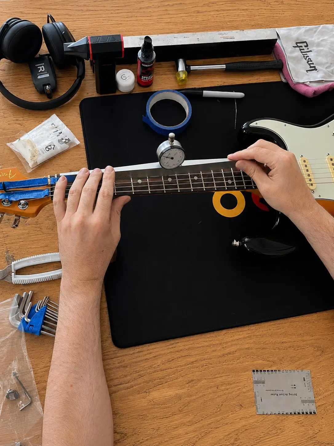 Dial gauge measuring neck relief on a black Stratocaster-style guitar